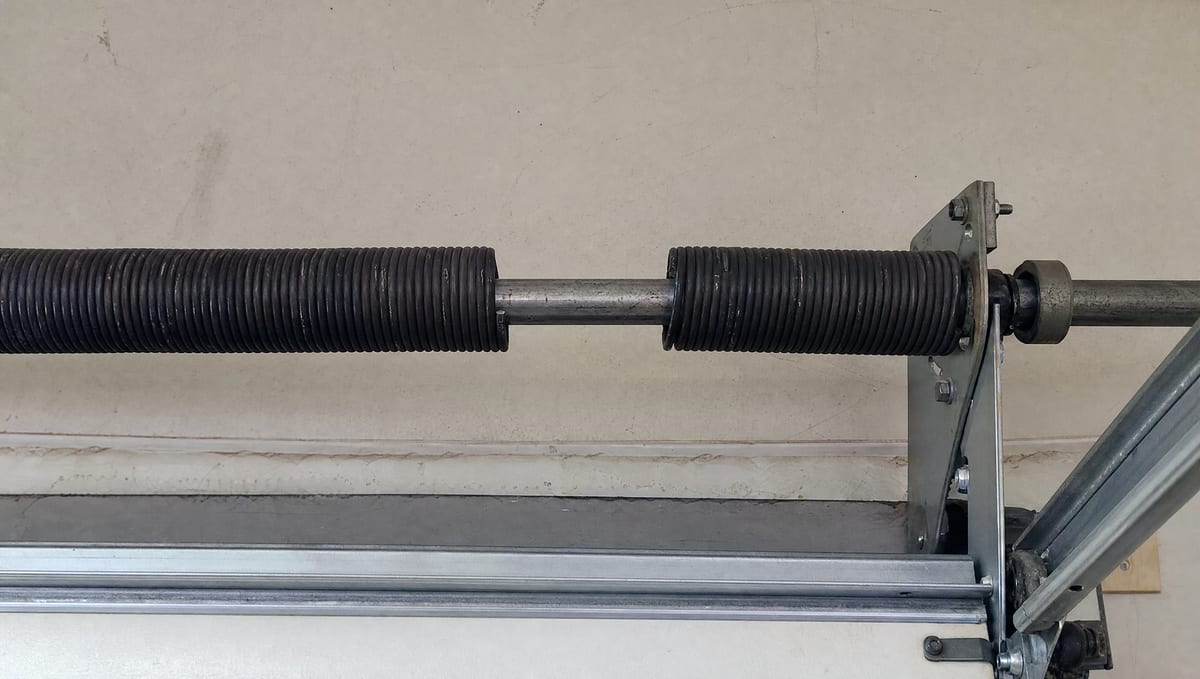 Close-up of a broken garage door torsion spring with a visible gap in the coil on the overhead shaft